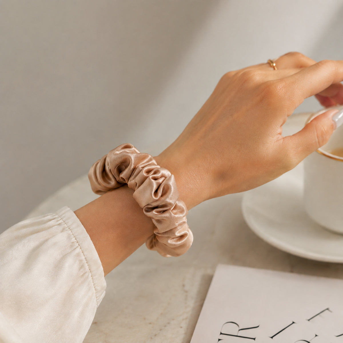 Large champagne Silk Scrunchie worn on the wrist, hand holding a coffee cup